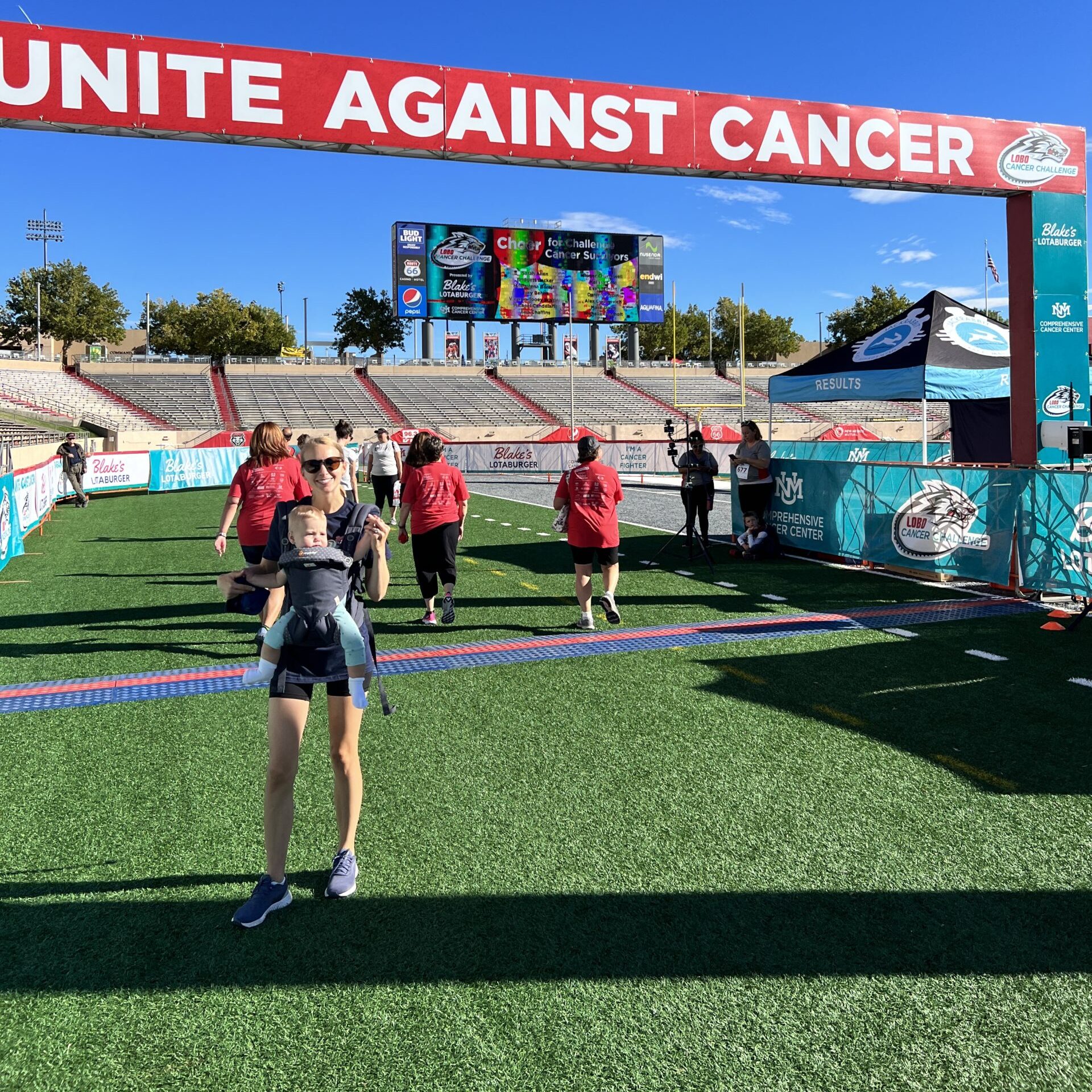 Team members of Blake's crossing a finish line while one poses for camera with baby