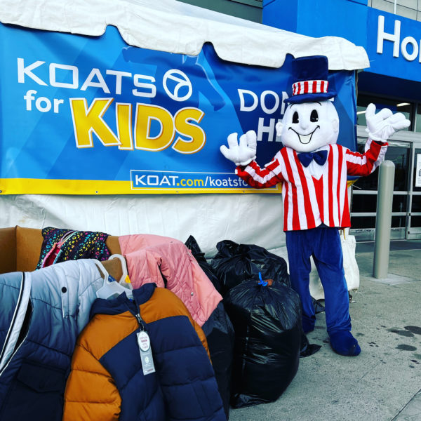 Blake's Lottaburger mascot standing in front of bags of coat donations