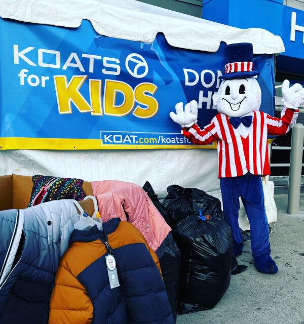 Blake's Lottaburger mascot standing in front of bags of coat donations