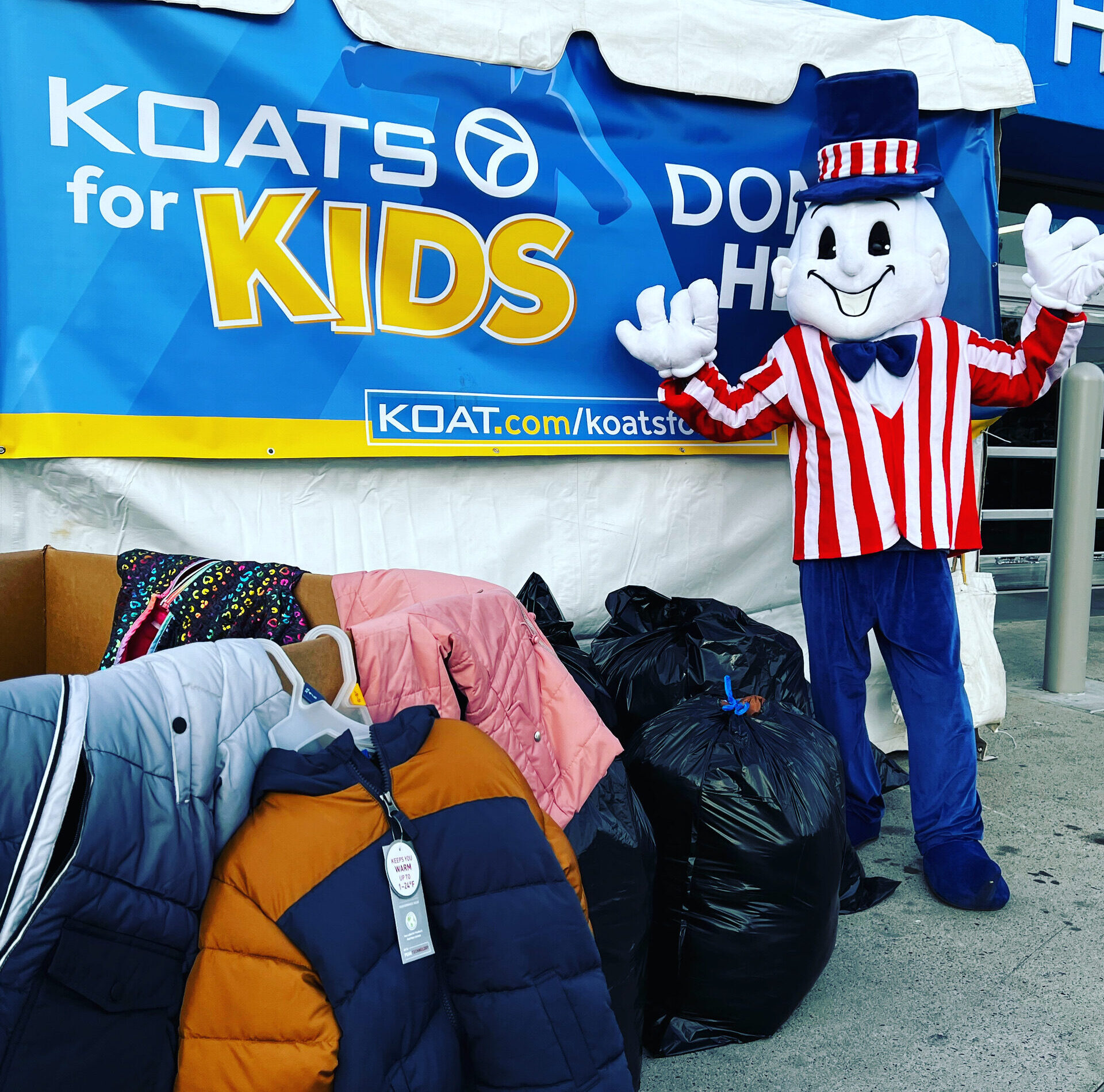 Blake's Lottaburger mascot standing in front of bags of coat donations