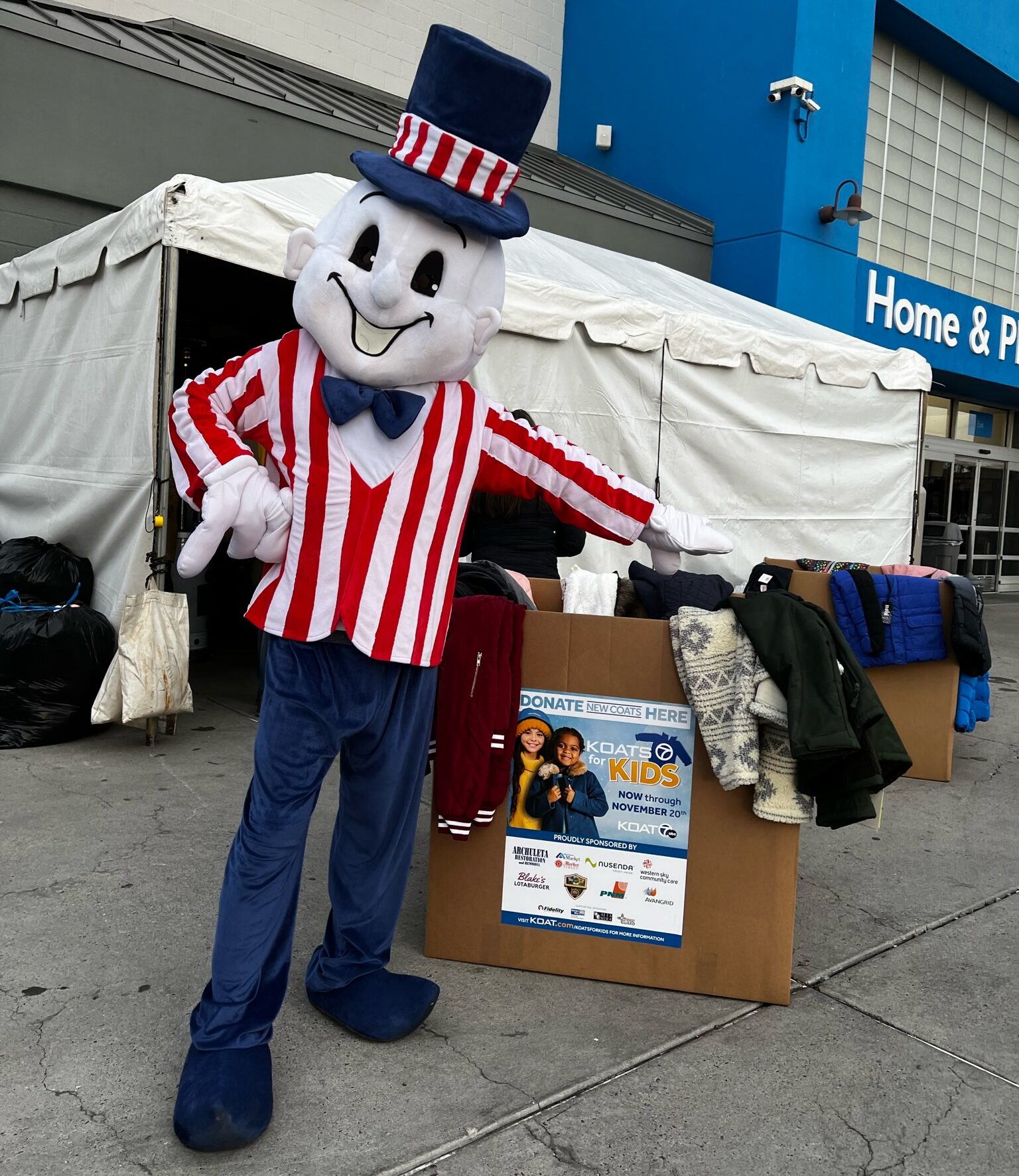 Blake's Mascot standing in front of a box filled with coat donations.