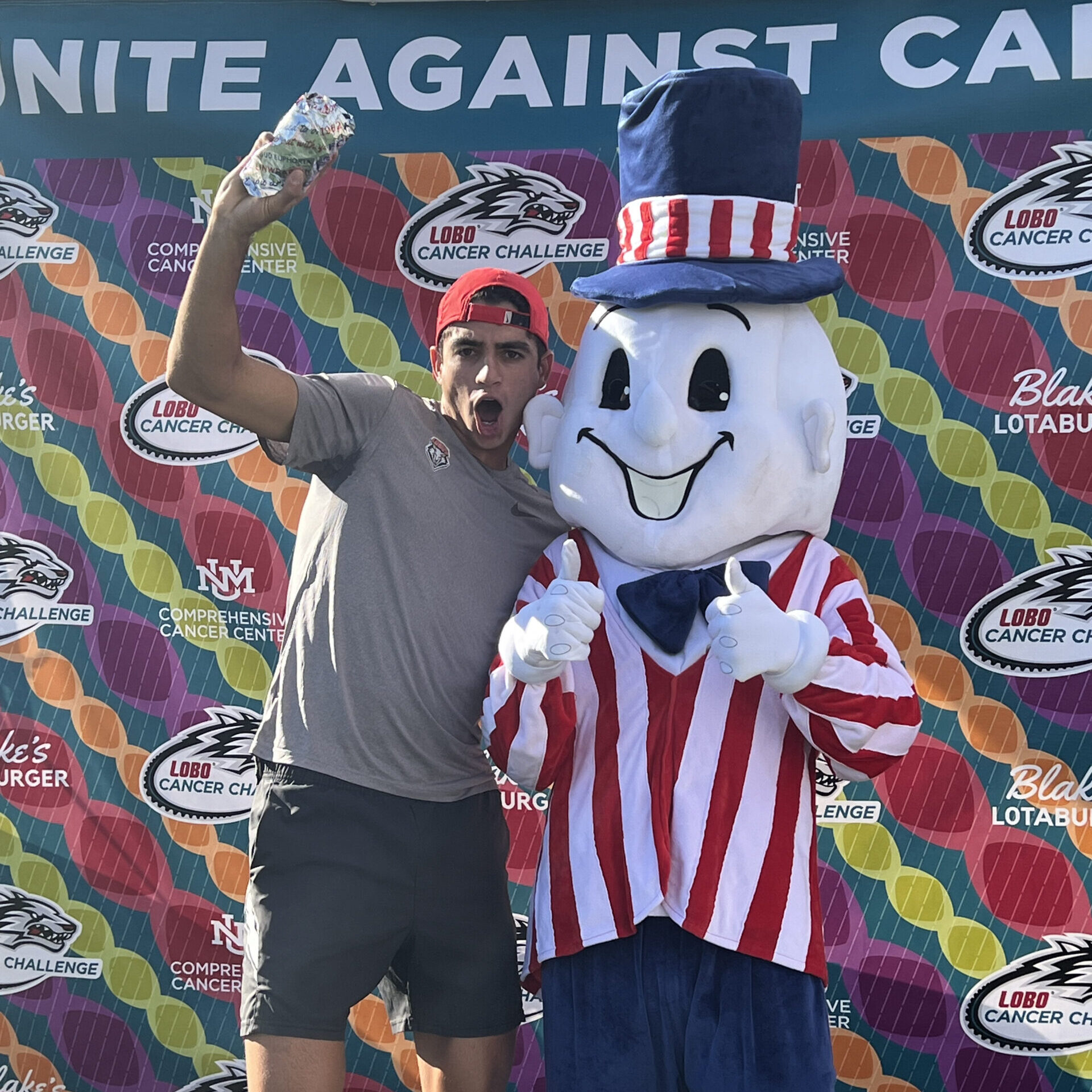 Someone getting their photo taken with Blake's mascot in front of a United Against Cancer backdrop