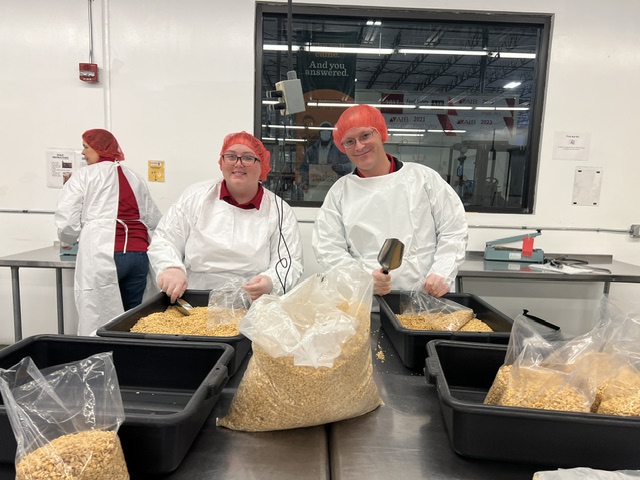 Blake's team members packing food at Road Runner Food Bank with hairnets and coveralls.