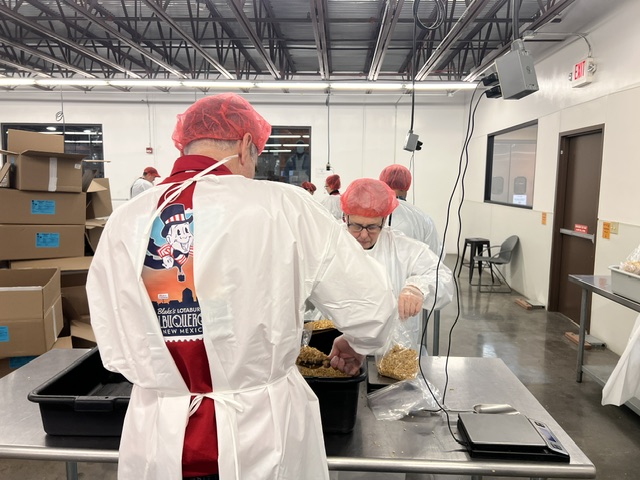 Blake's team members packing food at Road Runner Food Bank with hairnets and coveralls.