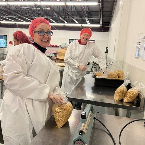 Blake's team members packing food at Road Runner Food Bank with hairnets and coveralls.