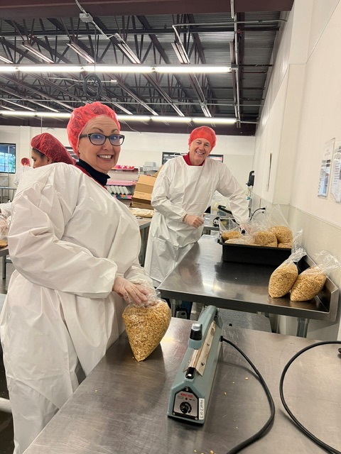 Blake's team members packing food at Road Runner Food Bank with hairnets and coveralls.